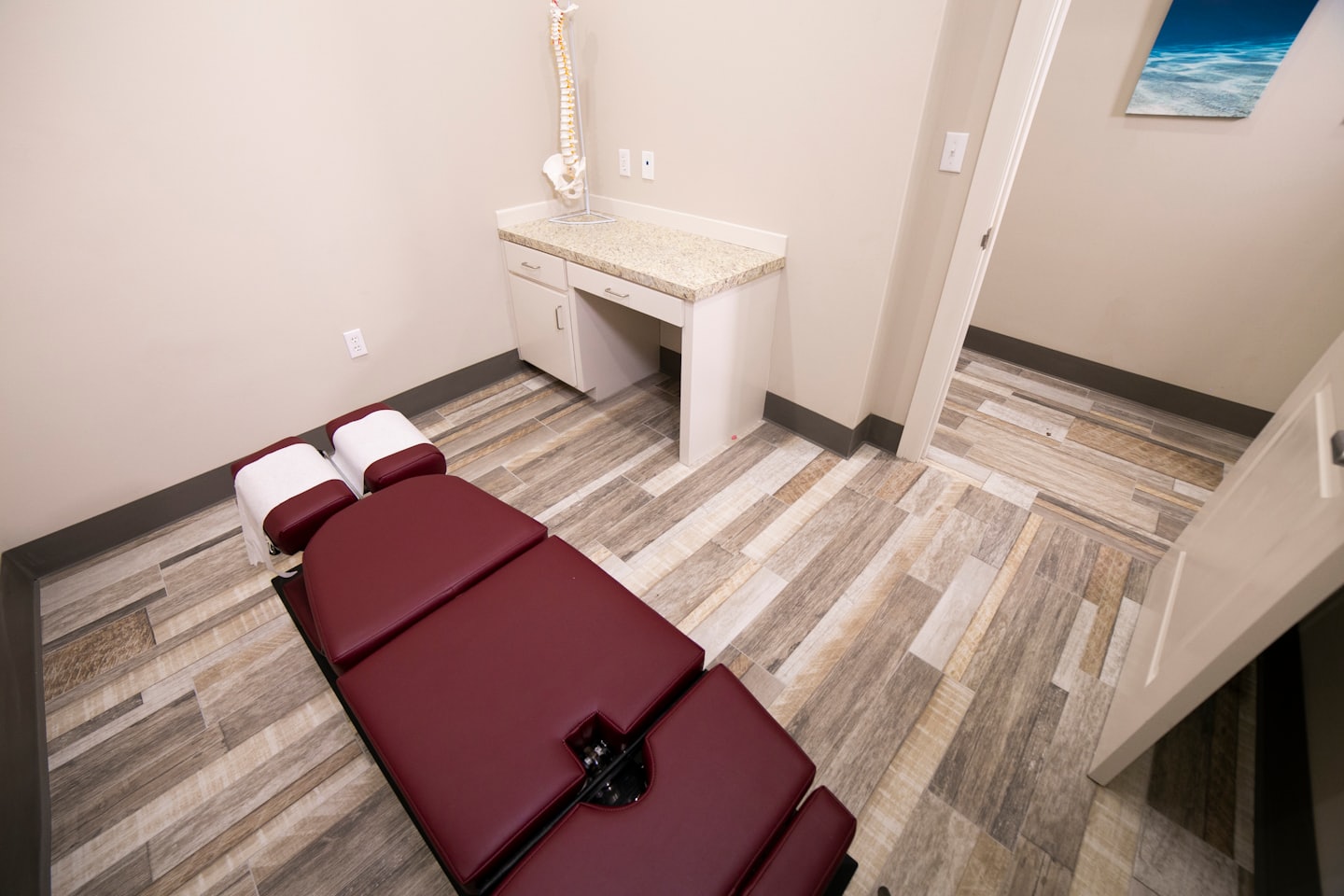 Sala di esame chiropratico con lettino color bordeaux e modello di colonna vertebrale.